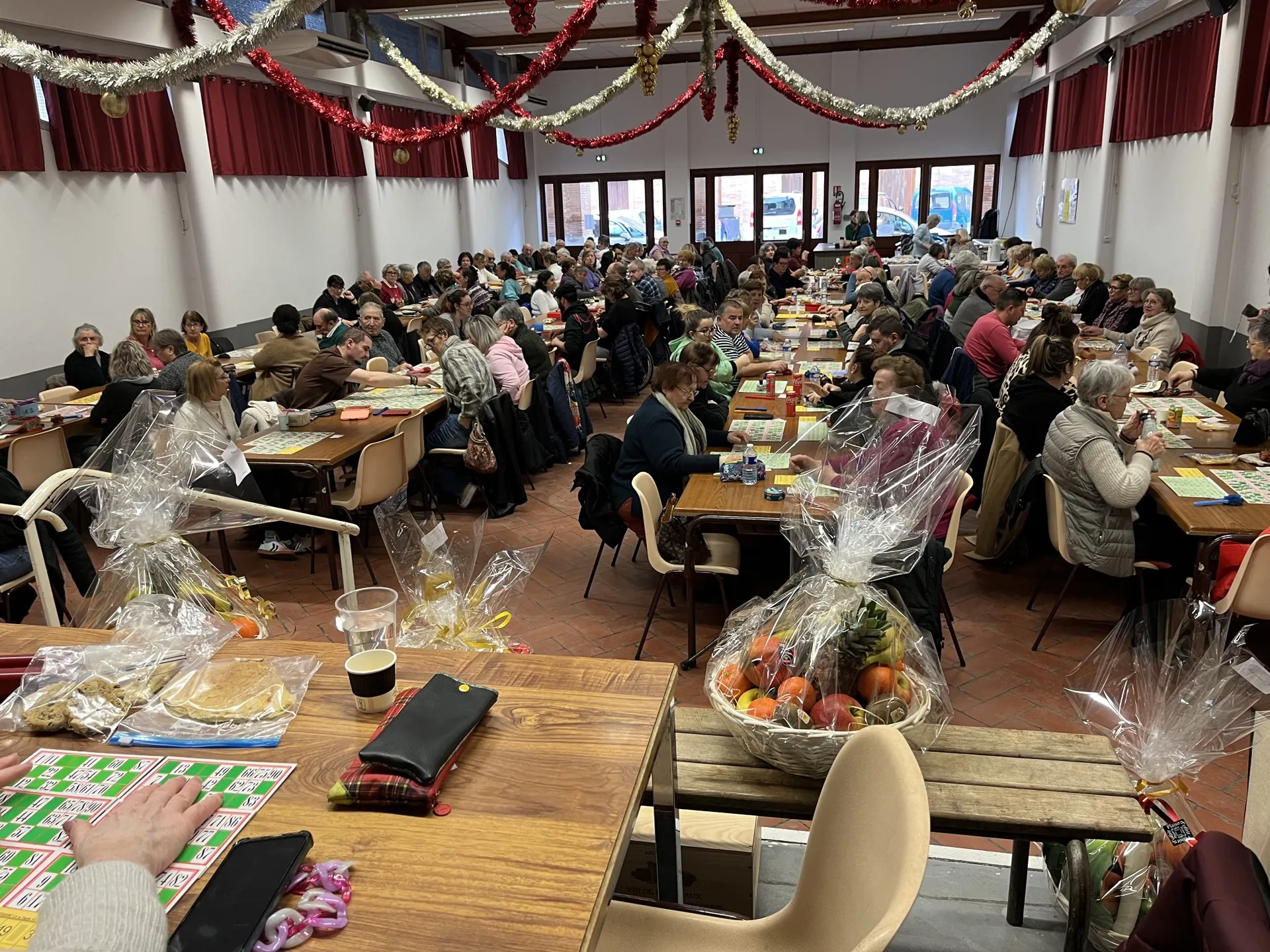 Salle comble au loto de l’association, cartons et paniers garnis sur les tables